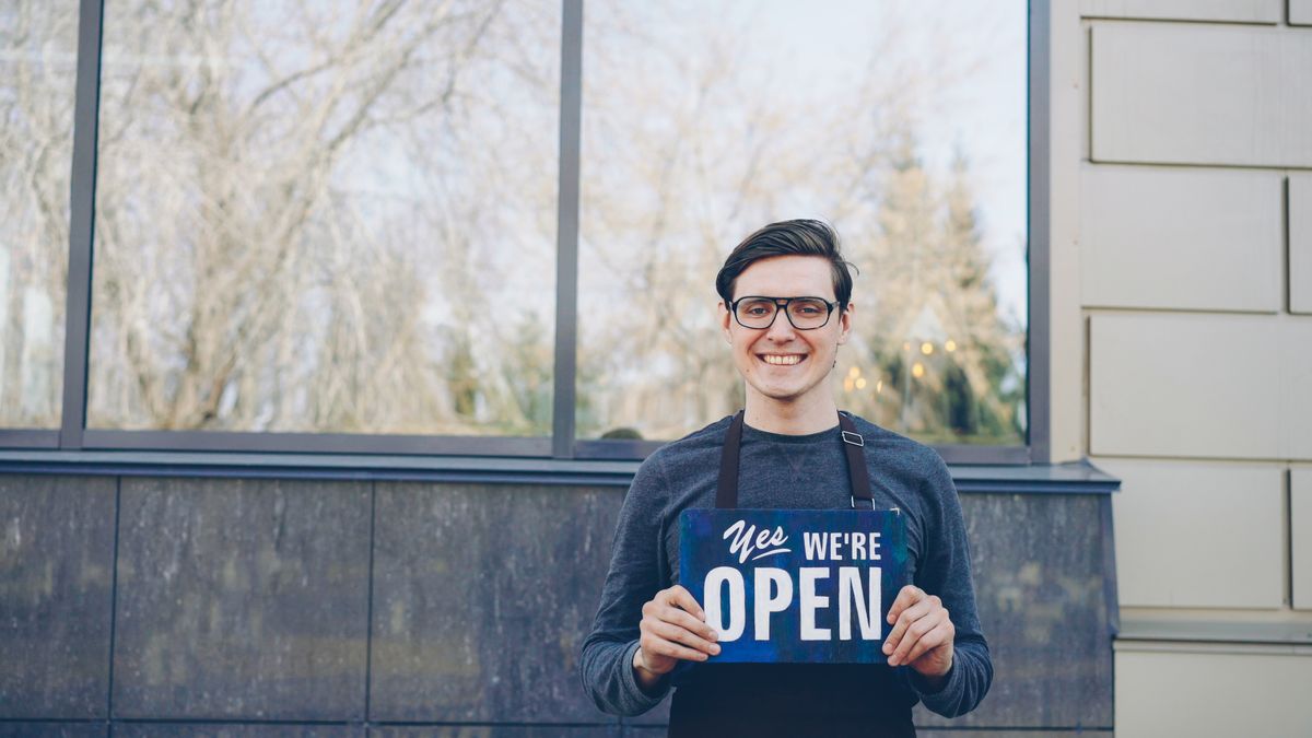 An independent shop owner smiling outside their store